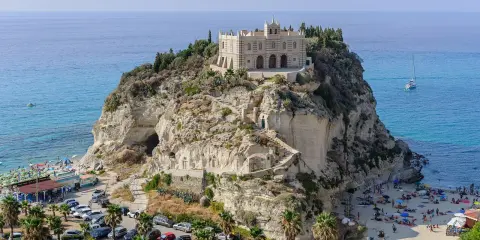 Santuario di Santa Maria dell'Isola a Tropea, regione Calabria, su uno sperone roccioso a picco sul mare azzurro, con spiaggia e palme.