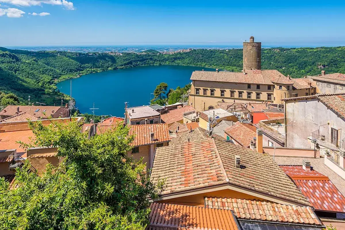 Vista panoramica di un borgo con tetti rossi affacciato su un lago blu, uno dei tanti paesi da vedere vicino Roma per una gita fuori porta.