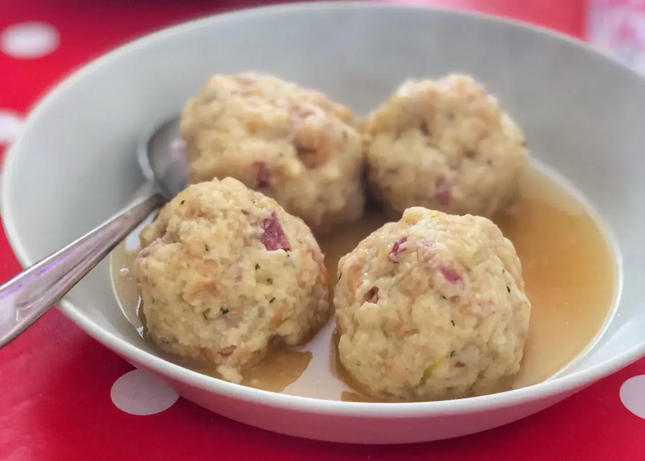 Canederli in brodo, un classico dei piatti tipici del Trentino Alto Adige, serviti in una ciotola bianca su un tavolo a pois rossi.