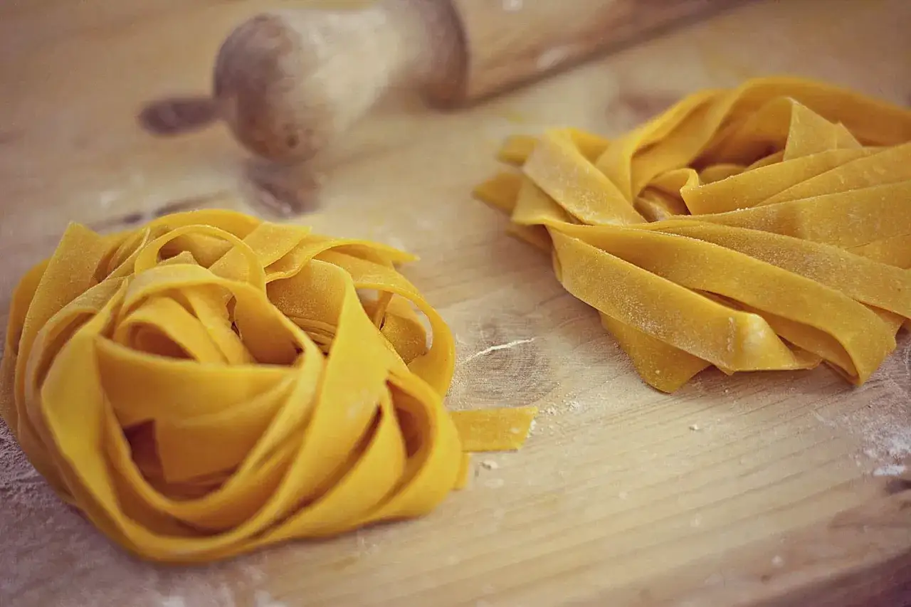 Fettuccine fresche su tagliere di legno, pronte per essere cucinate. Un assaggio di cosa mangiare a Forl&igrave;, con un mattarello sullo sfondo.